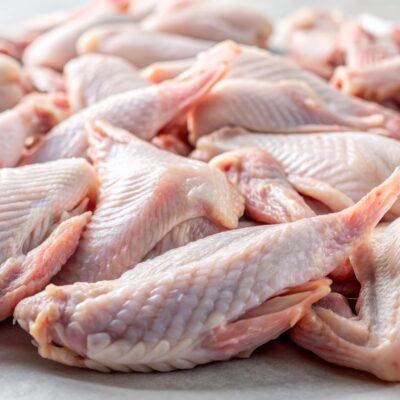 freshly purchased raw chicken wings with skin on, scattered on a white surface, glistening with moisture, waiting to be cooked or seasoned for a savory meal.
